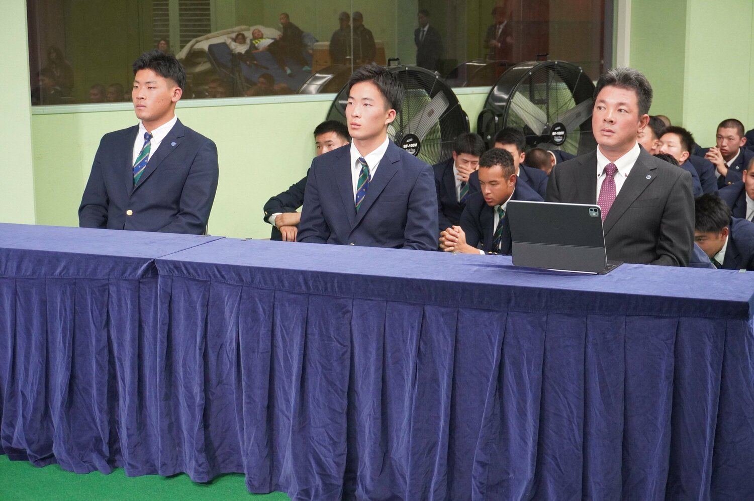 10月23日、仙台育英高校。ドラフト会議のテレビ中継を見つめる須江航監督。プロ野球志望届を提出していた3年生の高田庵冬(左)と吉川陽大(中央)。後ろでは野球部員が祈るように手を合わせる ©Kei Nakamura