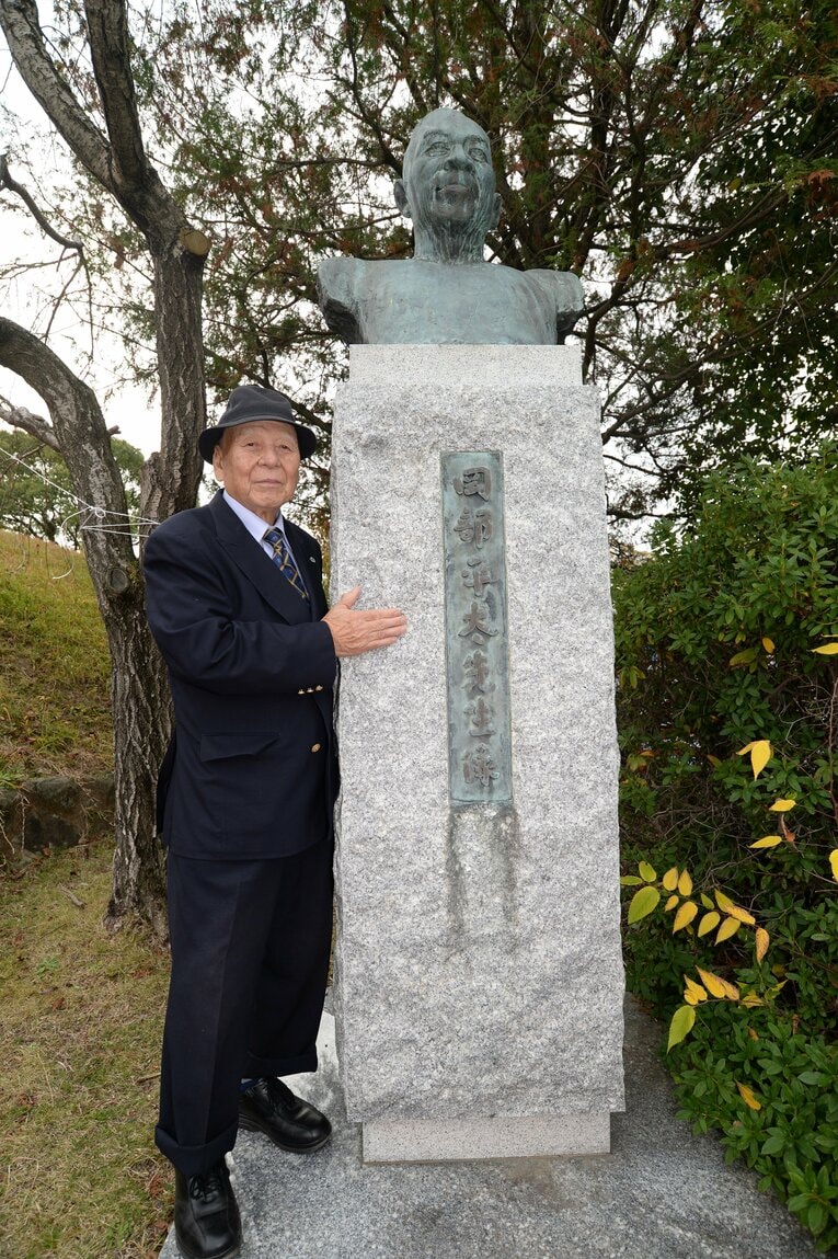 福岡市の平和台陸上競技場にある岡部平太の胸像前で写真に収まる生前の田中茂樹　©Koh Tanaka