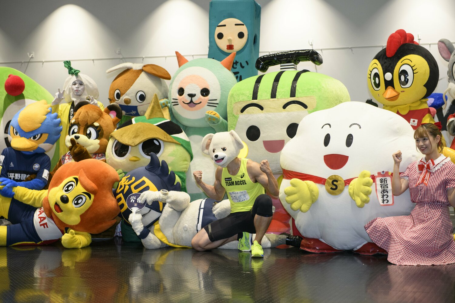 黄色いタンクトップ姿のマッスル根岸。ふわふわとしたゆるキャラに囲まれマッスルボディが一際目立つ　©Hirofumi Kamaya