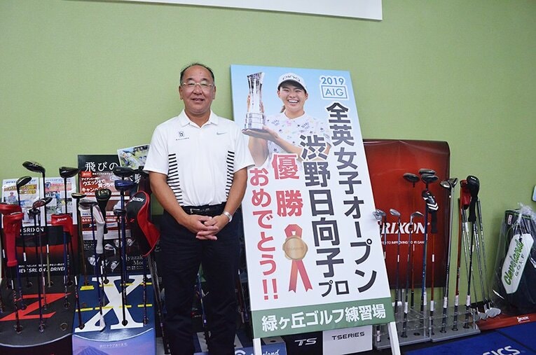 作陽高校ゴルフ部の田渕潔監督。支援者が作成したという記念看板とともに笑顔で写真に収まった。 ／ photograph by Toshihide Ishikura