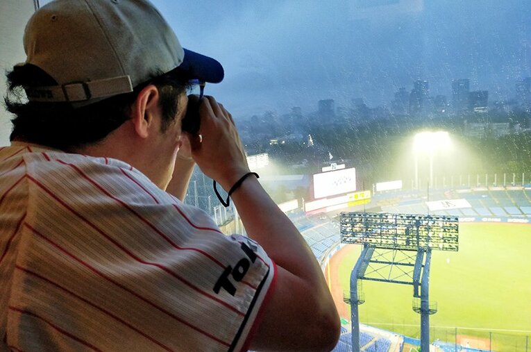 双眼鏡を通して試合を見守る長谷川氏。一塁側ヤクルトベンチが丸見えでファンにとっても嬉しい眺望だ。 ／ photograph by Sports Graphic Number