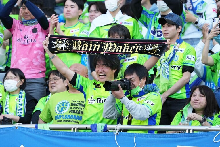 笑顔でレインメーカータオルを掲げるアウェイの湘南サポーター