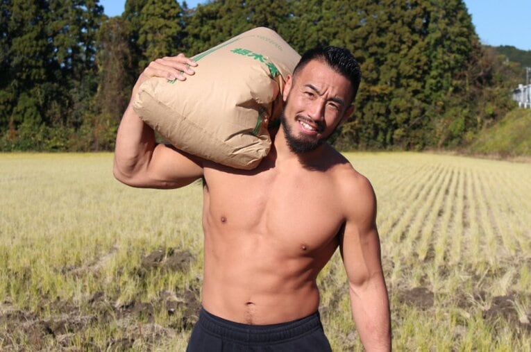 実家の田んぼで収穫した米を担ぐ手塚裕之。筋骨隆々の肉体はこの「米」によって作られた ／ photograph by Number Web