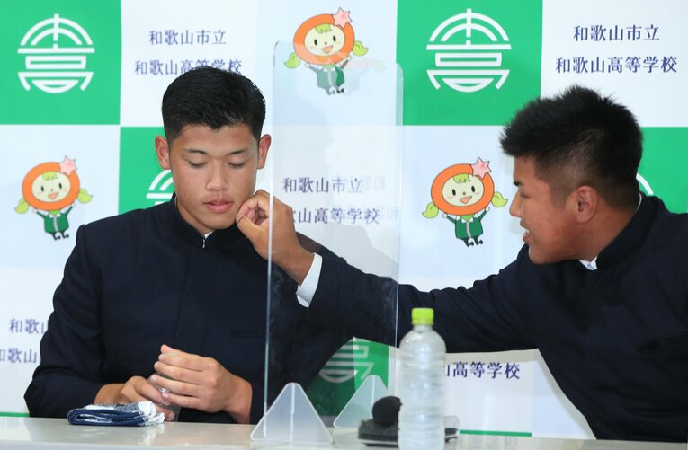 ともに市立和歌山高からドラフト１位指名を受け臨んだ記者会見中、小園健太投手（DeNA）の顔についたものを取る松川虎生捕手（ロッテ）©︎JIJI PRESS