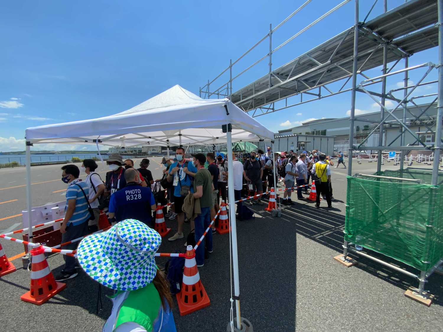 炎天下のなかバスを待つ人々。屋根はあるものの待っている人全員を覆うほどの大きさはない