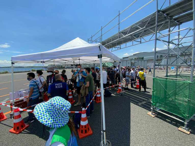 炎天下のなかバスを待つ人々。屋根はあるものの待っている人全員を覆うほどの大きさはない