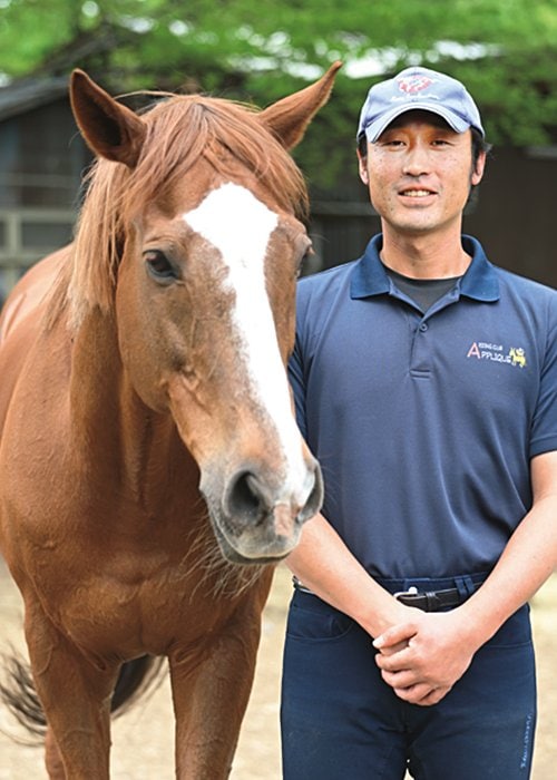 小学5年生から65歳まで乗馬を楽しめるアップリケ牧場の粕谷代表。隣はインティライミと同じくスペシャルウィーク産駒である「ウィーク」