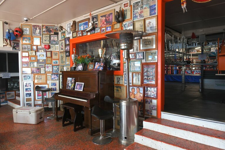 ジムの入口正面にはアップライトのピアノが置かれ、壁一面に過去の選手たちの写真や記事が張ってある　©Kokou Sekine