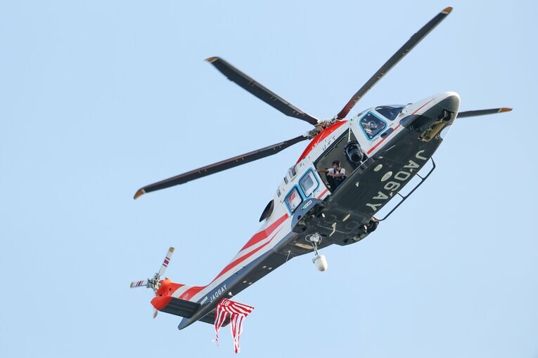 始球式のボールを運んできたヘリコプター。1回目、ボールは落下せず失敗。2回目で成功した（写真中央下、ボールは朝日新聞の社旗にくくりつけられている）